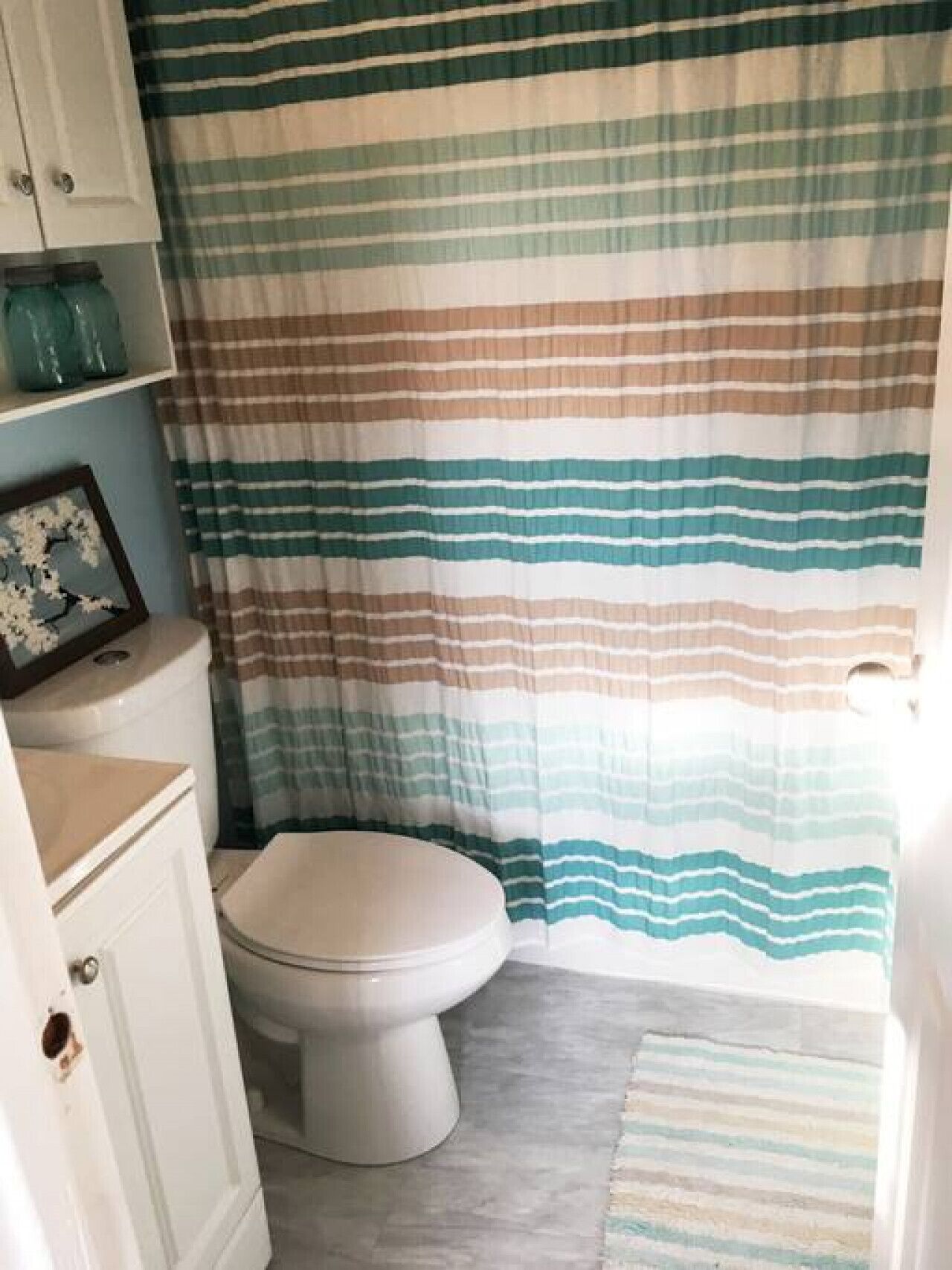 A bathroom with a striped shower curtain, a toilet, a sink, and a framed picture on the wall.