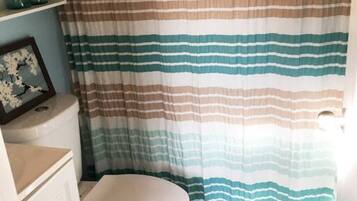 A bathroom with a striped shower curtain, a toilet, a sink, and a framed picture on the wall.