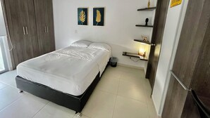 Ein Schlafzimmer mit Bett, Kleiderschrank, zwei gerahmten Blätter-Kunstwerken, einem Nachttisch mit Lampe und einer Tür mit 'New York' Schriftzug.