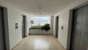 Ein moderner Flur mit zwei Aufzügen, einem großen Fenster mit Blick auf die Stadt und einem Pflanzenbeet.