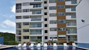 Ein mehrstöckiges Hotel mit Schwimmbad und Liegestühlen.