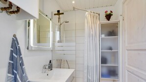 A modern bathroom with a shower, a sink, a toilet, and a mirror. There is a towel hanging on the wall and a small plant on the shelf.