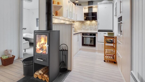 A modern kitchen with a wood-burning stove, white cabinetry, and a dining area with a wooden table.