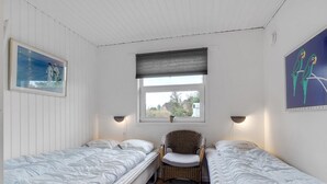 A room with two single beds, a wicker chair, a window with a view, and wall art.