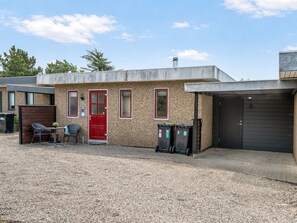 A building with a red door, windows, and a garage door. There are two trash bins and a table with chairs outside. - "Sighmar" - 900m from the sea by Interhome (Blåvand)