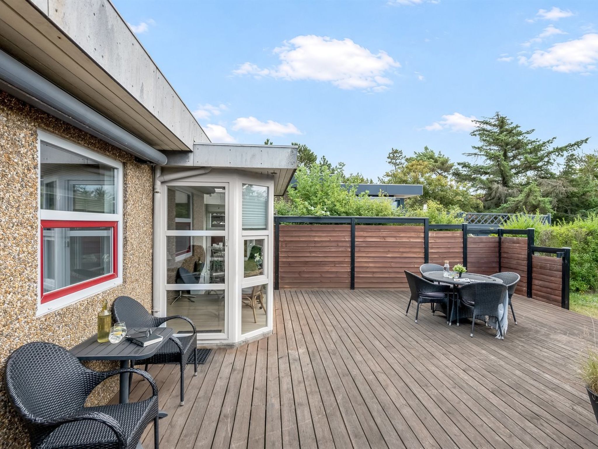 Eine Terrasse mit Gartenmöbeln, ein Glastür-Eingang und ein Holzzaun.
