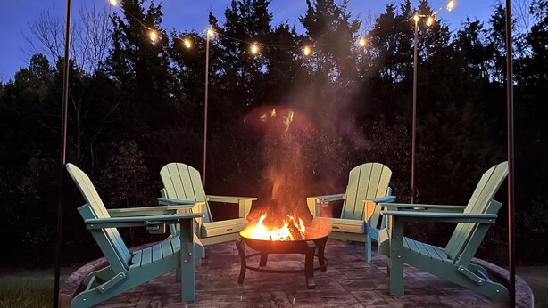 A fire pit with two Adirondack chairs facing it, surrounded by stone tiles and string lights.