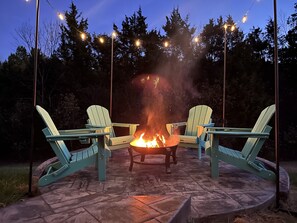 Una chimenea rodeada de losa, con dos sillas Adirondack apuntando hacia ella, y luces colgantes.