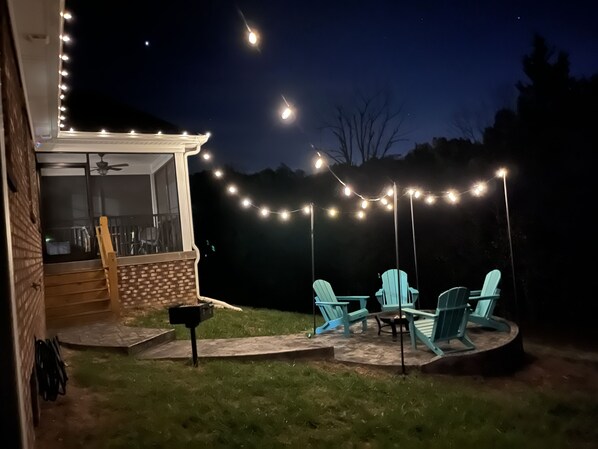 Un patio trasero con mobiliario exterior, luces colgantes y un muro de ladrillo.