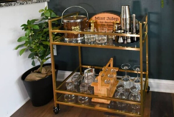 A gold-framed bar cart with a sign reading "Mint julep," containing a wooden bucket, a shaker, and various glassware.
