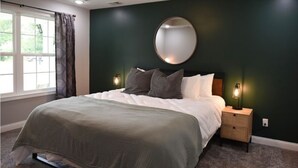 A bedroom with a large bed, dark green walls, a round mirror above the bed, and two bedside lamps.
