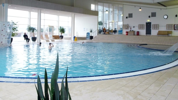Une piscine intérieure avec un toboggan, des espaces de détente et de grandes fenêtres.