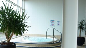 Un espace dédié à un bain à remous, agrémenté d’une grande plante en pot, d’un sol carrelé et d’un escalier en métal menant au bain.