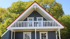 Une maison à deux étages avec un balcon, de grandes fenêtres et une véranda à l’avant, équipée de chaises.