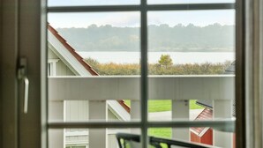 Une vue à travers une fenêtre à carreaux, donnant sur une étendue d’eau et une ligne d’arbres à l’horizon.