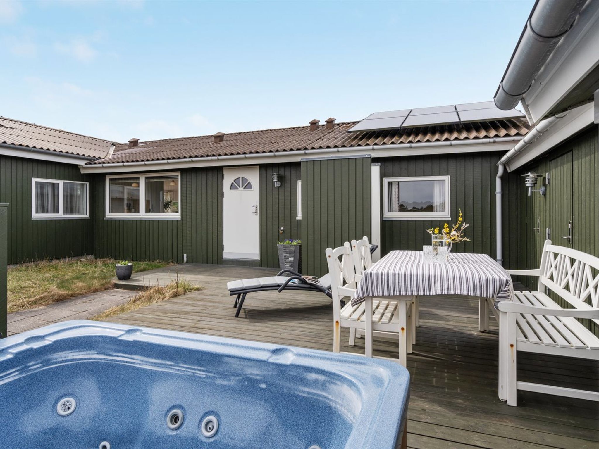 Een gezellig buitengebied met een jacuzzi, een tafel met stoelen en uitzicht op een groen gebouw met ramen en een deur.