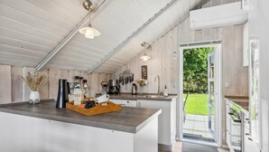 Et moderne køkken med en central ø, træskabe og et stort vindue med udsigt til naturen.