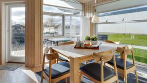 Ein moderner Essbereich mit einem Holztisch und Stühlen, großen Fenstern und Blick ins Freie.