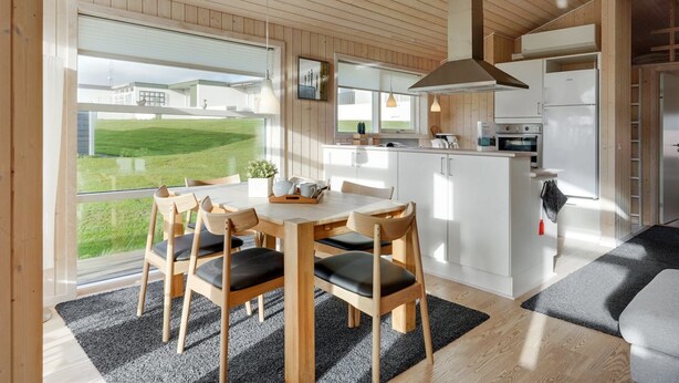 Eine moderne Küche mit weißen Schränken, einem Edelstahlkühlschrank und einem großen Fenster mit Blick auf eine grüne Landschaft.