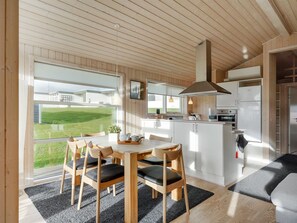 Una cocina moderna con armarios blancos, un refrigerador de acero inoxidable y un amplio ventanal con vistas a un paisaje verde.