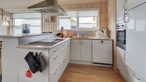Eine moderne Küche mit Holzausstattung, einem eingebauten Backofen und einer großen Kochinsel mit Herd und Spüle.