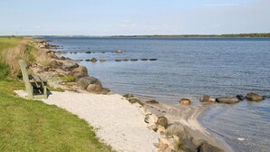 A coastal path with a wooden bench, gravel, and scattered rocks leading to a calm sea. - "Ilya" - 90m to the fjord by Interhome (Storvorde)