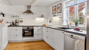 Een moderne keuken met witte kasten, een inbouwoven, een Bosch vaatwasser en een raam met uitzicht op een geel gebouw.