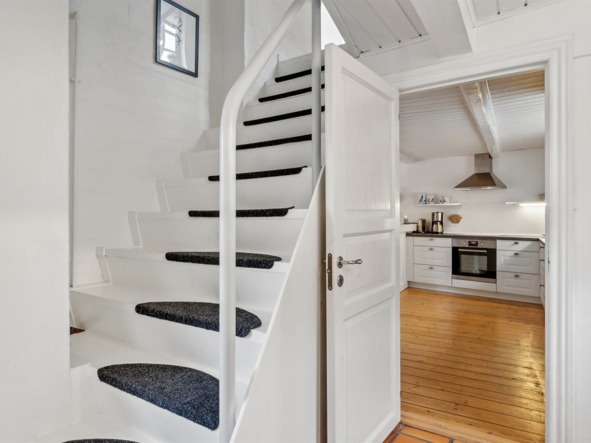 Un escalier dont les marches sont recouvertes d’un tapis noir, menant à une porte blanche.