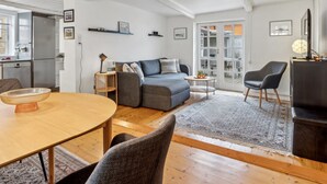 Een ruime zithoek met een grijze bank, een houten eettafel en een zwarte fauteuil.