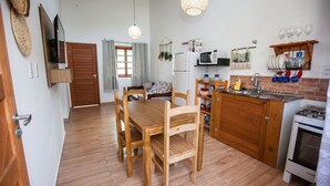 A compact kitchen with wooden furniture, a microwave, a stove, and a dining area with chairs. - Paraíso em Balneário Camboriú - Praia do Estaleiro by ReservaStar (Balneário Camboriú)