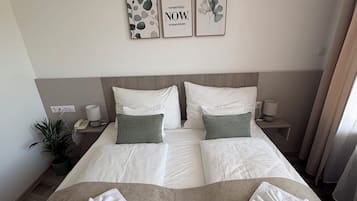 A double bed with white and green bedding, two towels, a bedside table with a lamp, and three framed pictures on the wall.
