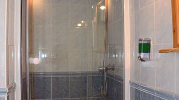 Ducha con puerta de cristal, bañera blanca y dispensador de jabón en la pared.