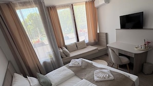 Una habitación de hotel con una cama, un escritorio, una silla, un televisor y ventanas grandes con cortinas.