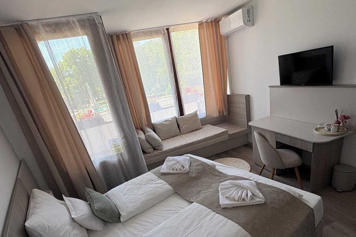 Ein Hotelzimmer mit Bett, Schreibtisch, Stuhl, Fernseher und großen Fenstern mit Vorhängen.