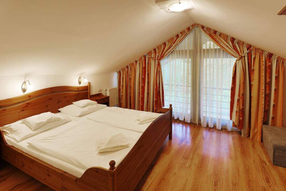 Ein Schlafzimmer mit einem hölzernen Bett, einem Nachttisch, einer Lampe und einem Fenster mit Vorhängen.
