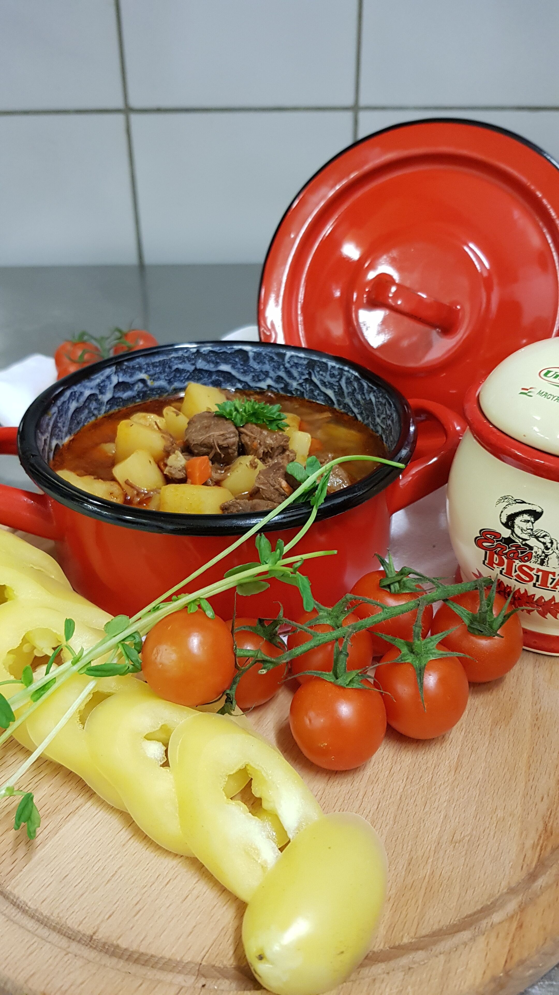 Una olla roja con estofado, una tabla de madera para cortar y verduras frescas.