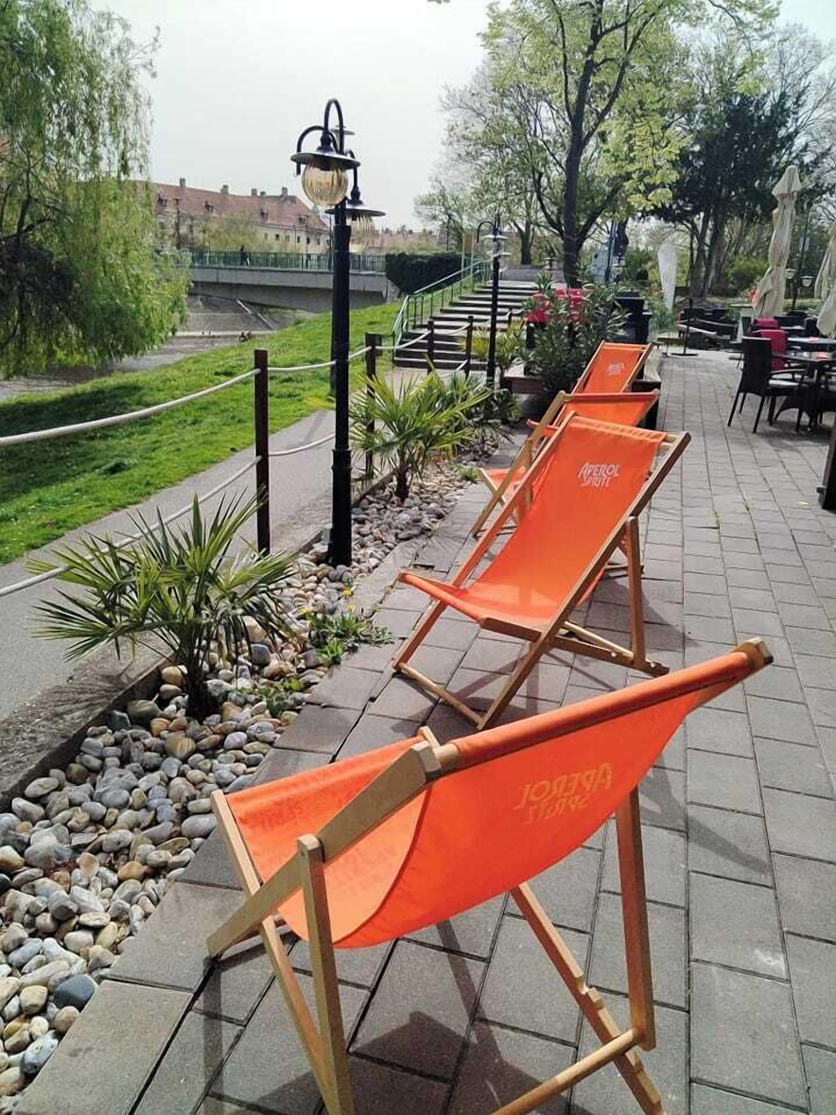Outdoor seating with orange chairs, a lamp post, and a pathway lined with plants and rocks.