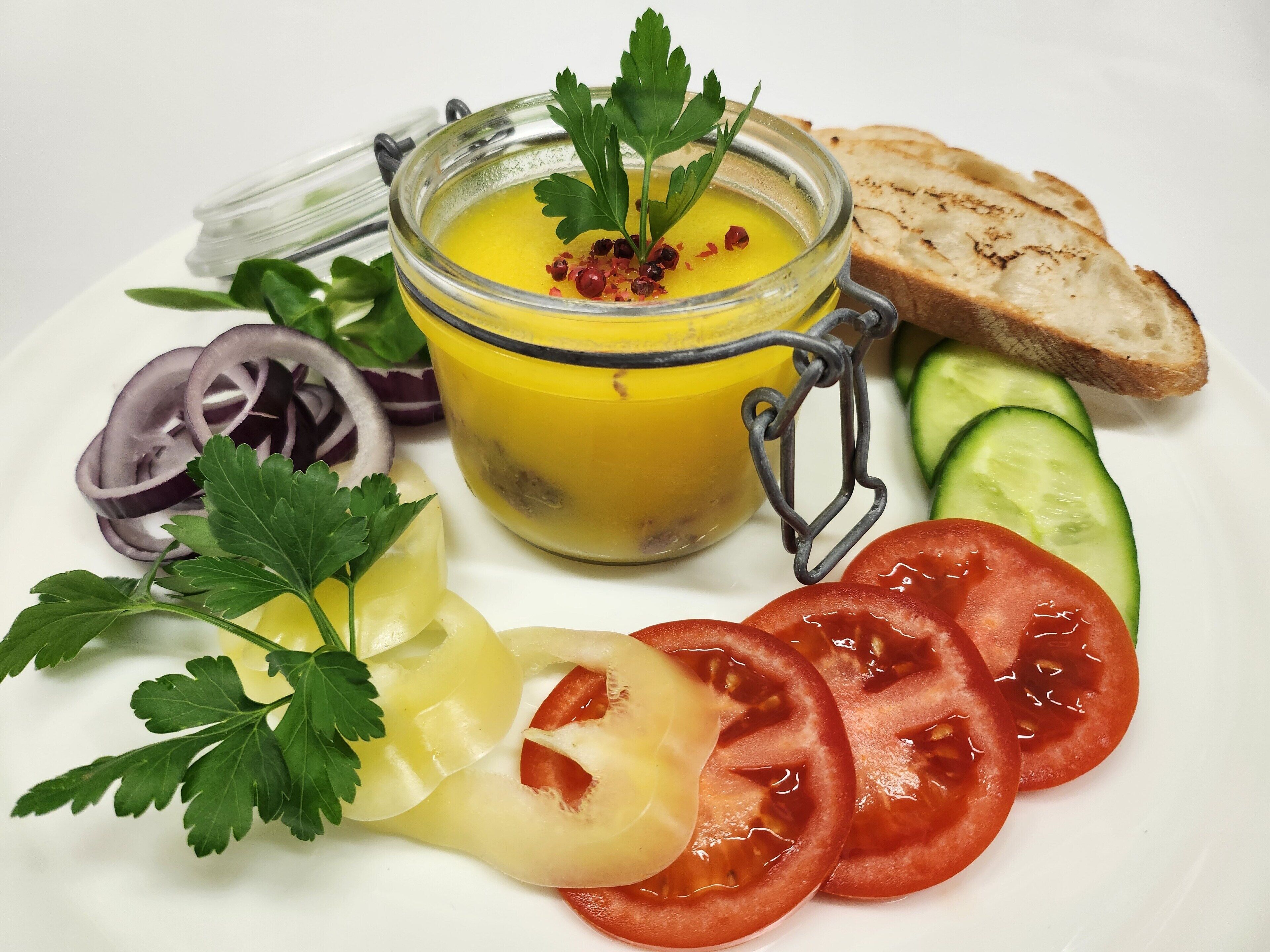 A plate with sliced tomatoes, cucumbers, red onions, and a jar of yellow sauce garnished with parsley.