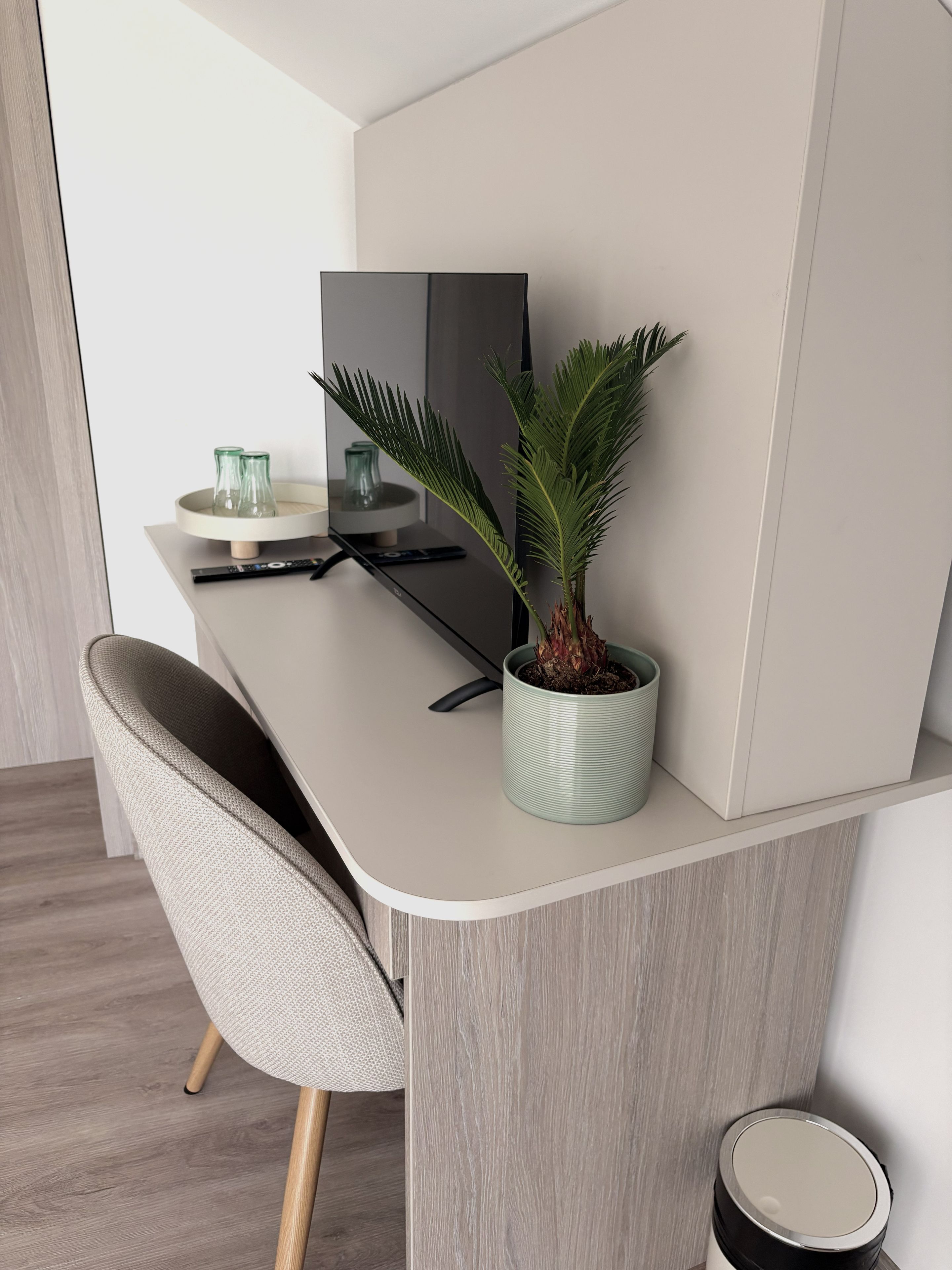 Escritorio moderno y minimalista con una planta en maceta, un control remoto y un recipiente de vidrio.