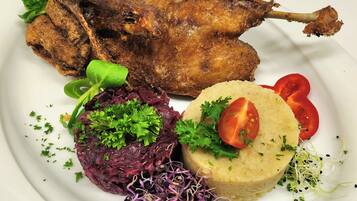 Un plato con pato asado, repollo morado, brotes y una guarnición de tomate.