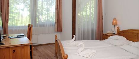 A neatly made bed with white linens and two swan-shaped towels, a wooden desk with a lamp, and a chair.