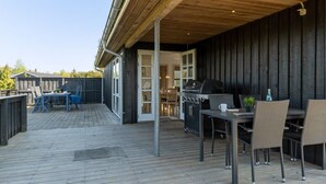 En udendørs terrasse med grill, spisebord og stole.