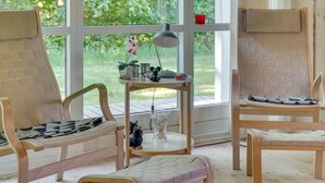 A room with two wooden chairs, a small table with decorative items, and a view of greenery through large windows. - "Elita" - 1.7km from the sea by Interhome (Hals)