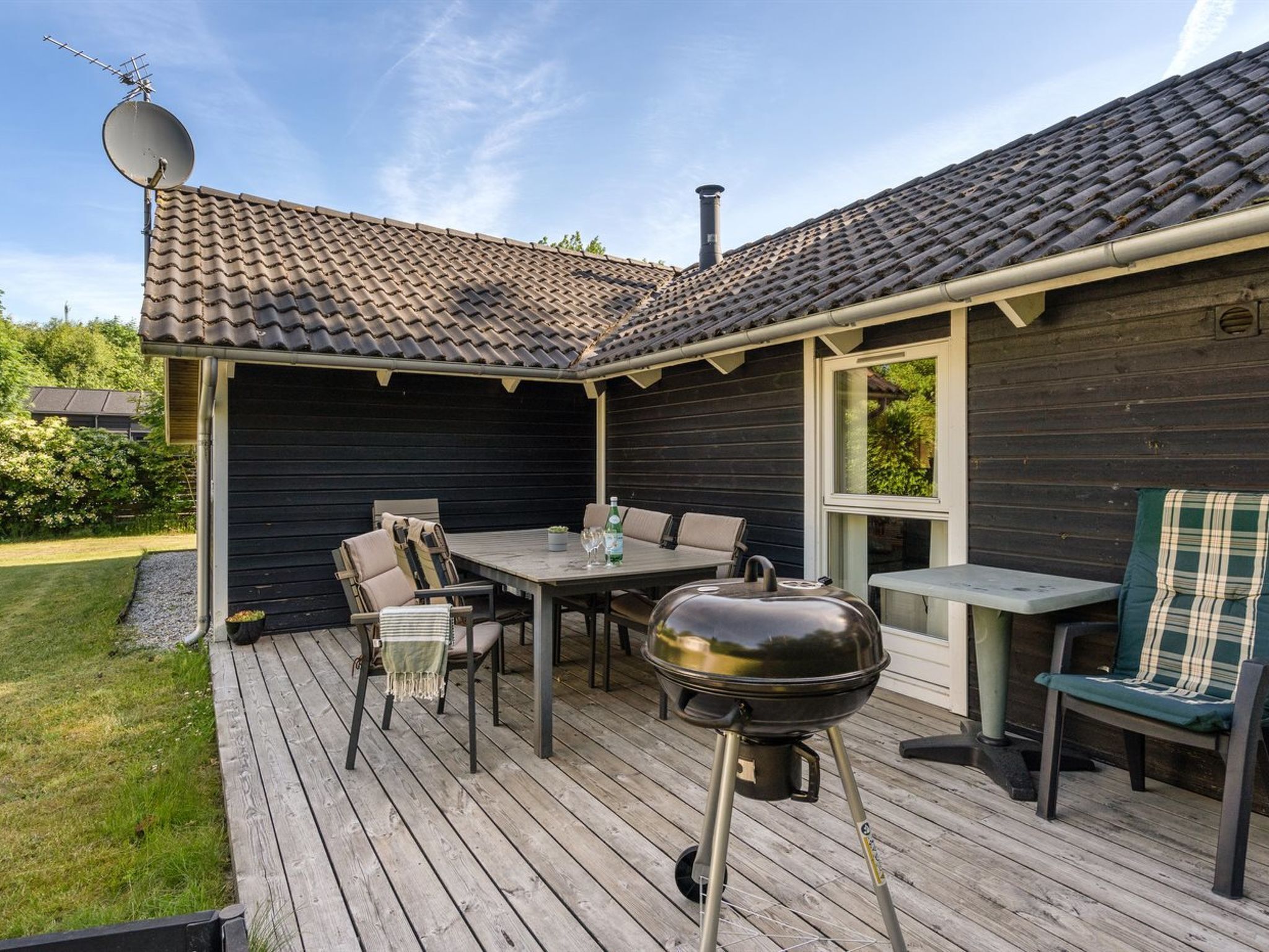 Een terras met een barbecue, eettafel en stoelen, omgeven door een donker houten huis.