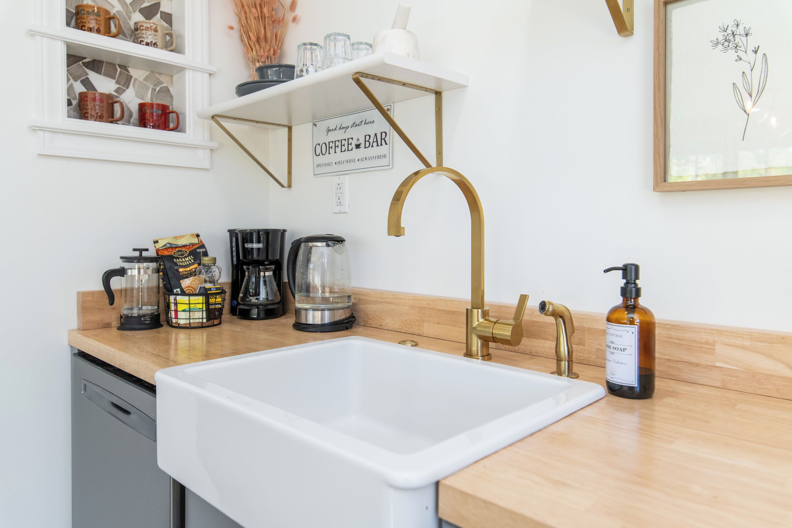 A kitchen with a white sink, a gold faucet, a coffee bar sign, and various kitchen appliances.