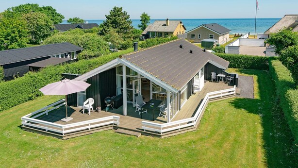 Une maison moderne dotée d’une véranda en verre, d’une terrasse et offrant une vue sur la mer.