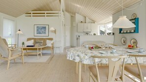 Une pièce spacieuse avec un plafond haut, un plancher en bois, un coin repas avec une table dressée pour quatre personnes et un coin salon confortable avec un canapé et des fauteuils.
