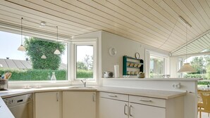 Une cuisine moderne dotée d’un îlot central, de meubles blancs et d’une grande fenêtre offrant une vue sur l’extérieur.