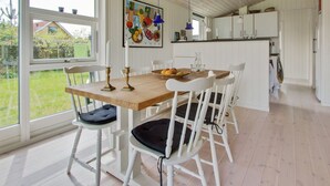 Une cuisine lumineuse avec des meubles blancs, une table en bois et une grande fenêtre donnant sur un jardin.