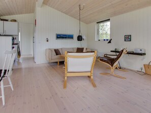 A spacious room with a wooden ceiling, a sofa, a dining table, and a chair.